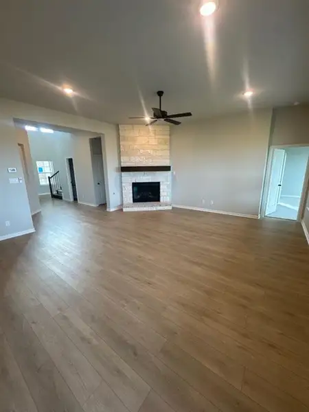 Spacious open-concept living area featuring wood-finish flooring, a stone-clad fireplace with a dark wood mantel, a ceiling fan, and recessed lighting