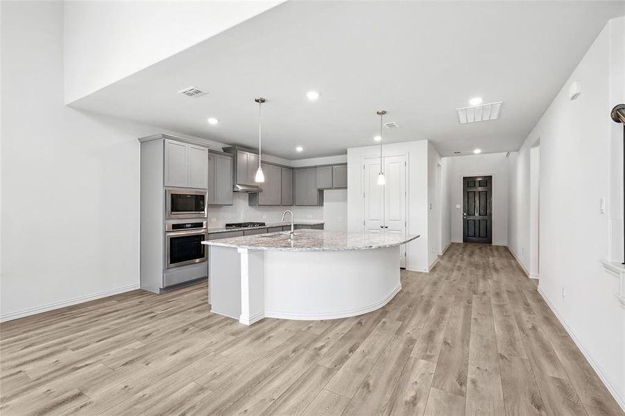 Kitchen with gray cabinetry, appliances with stainless steel finishes, light wood-type flooring, a kitchen island with sink, and recessed lighting Kitchen with gray cabinetry, appliances with stainless steel finishes, light wood-type flooring, a kitchen island with sink, and recessed lighting