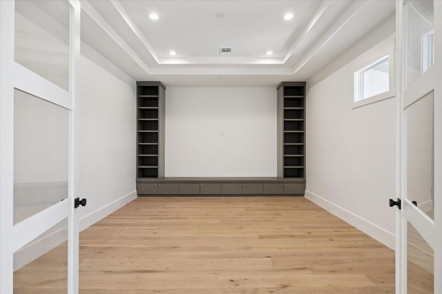 Media or theater room includes built-in shelves and storage cabinets, recessed lighting, and a tray ceiling, with glass French doors. Media or theater room includes built-in shelves and storage cabinets, recessed lighting, and a tray ceiling, with glass French doors.