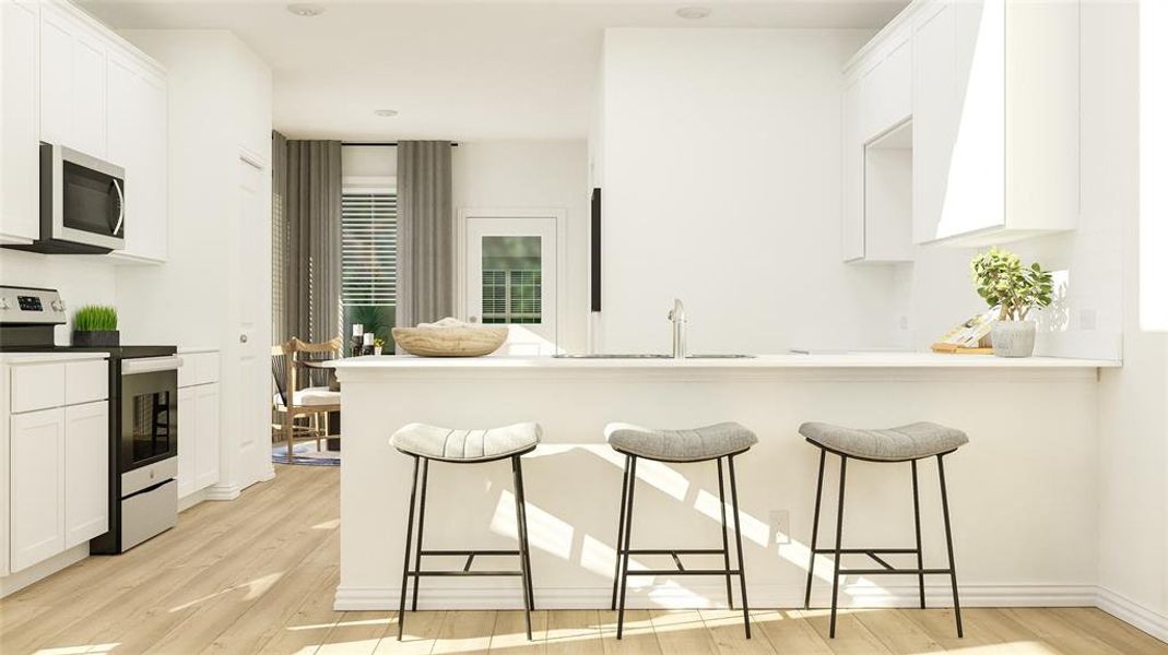 Kitchen with a kitchen bar, stainless steel appliances, sink, light hardwood / wood-style floors, and white cabinetry