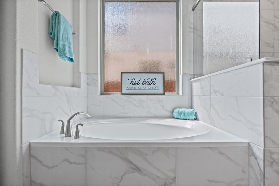 Indulge in a tranquil bathing experience with this built-in soaking tub, elegantly surrounded by polished marble-look tiling.