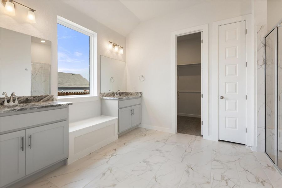 Full bath featuring light marble finish floors, two vanities, a marble finish shower, and a walk in closet