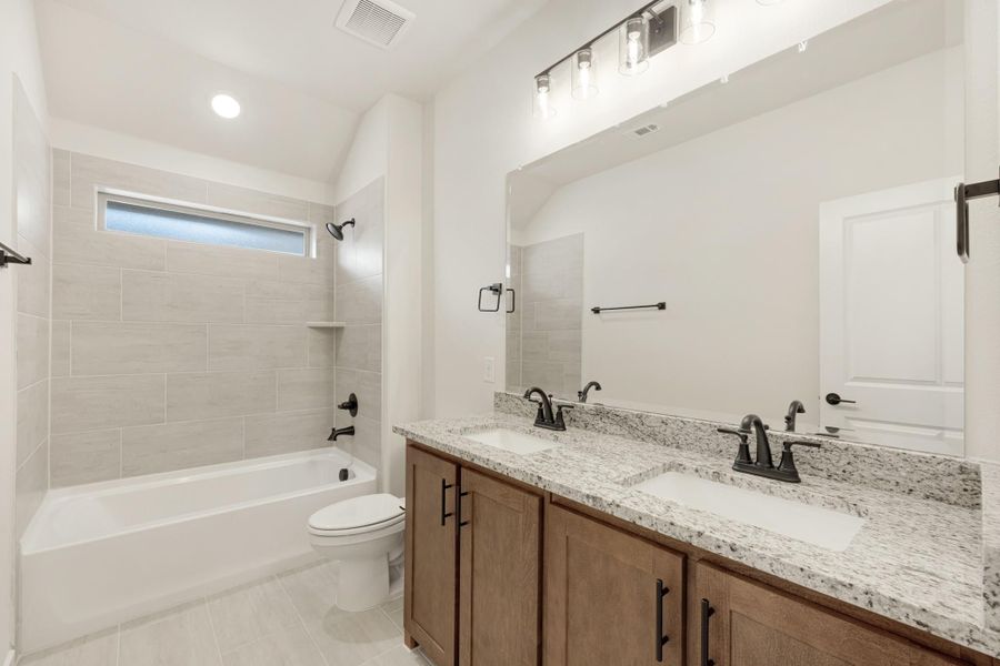 Bathroom with double sink vanity, granite countertop, tiled tub-shower combo, and wood cabinets with dark hardware