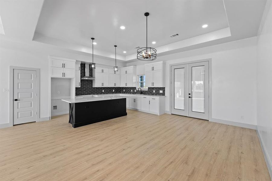Kitchen featuring dark cabinetry, white cabinets, hanging light fixtures, a raised ceiling, and recessed lighting
