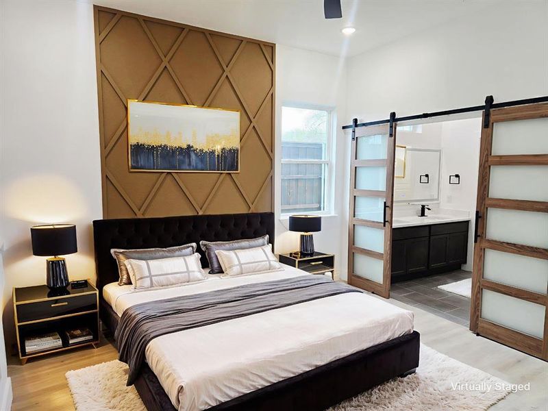 Bedroom with a barn door, light wood-style flooring, ceiling fan, and ensuite bath