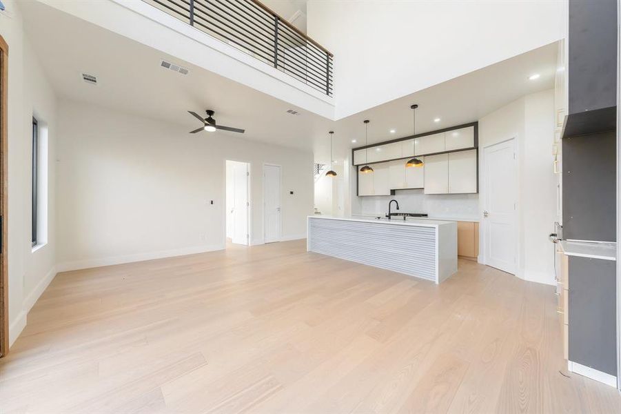 Unfurnished living room with light wood-style floors, a towering ceiling, a ceiling fan, and recessed lighting Unfurnished living room with light wood-style floors, a towering ceiling, a ceiling fan, and recessed lighting