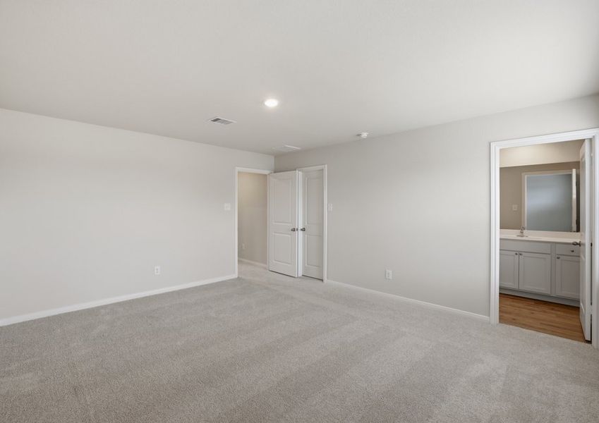 Primary bedroom featuring carpet flooring and a doorway leading into the ensuite primary bathroom.