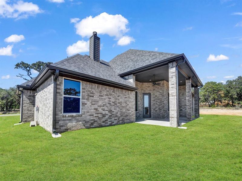 Back of house featuring a patio, a ceiling fan, a yard, a chimney, and brick siding