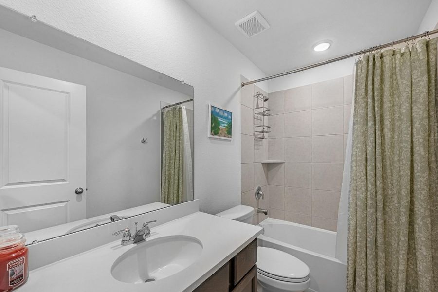 The secondary bath features tile flooring, custom stained cabinetry and light countertops and a shower/tub combo. Perfect for accommodating any visiting family and friends.