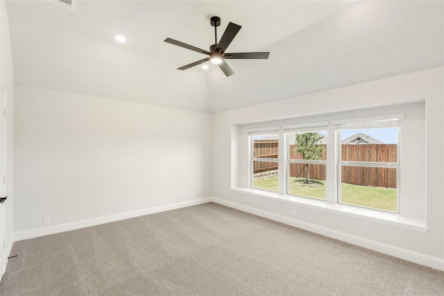Empty bedroom with vaulted ceiling, ceiling fan, carpet flooring, and large window overlooking backyard fence Empty bedroom with vaulted ceiling, ceiling fan, carpet flooring, and large window overlooking backyard fence