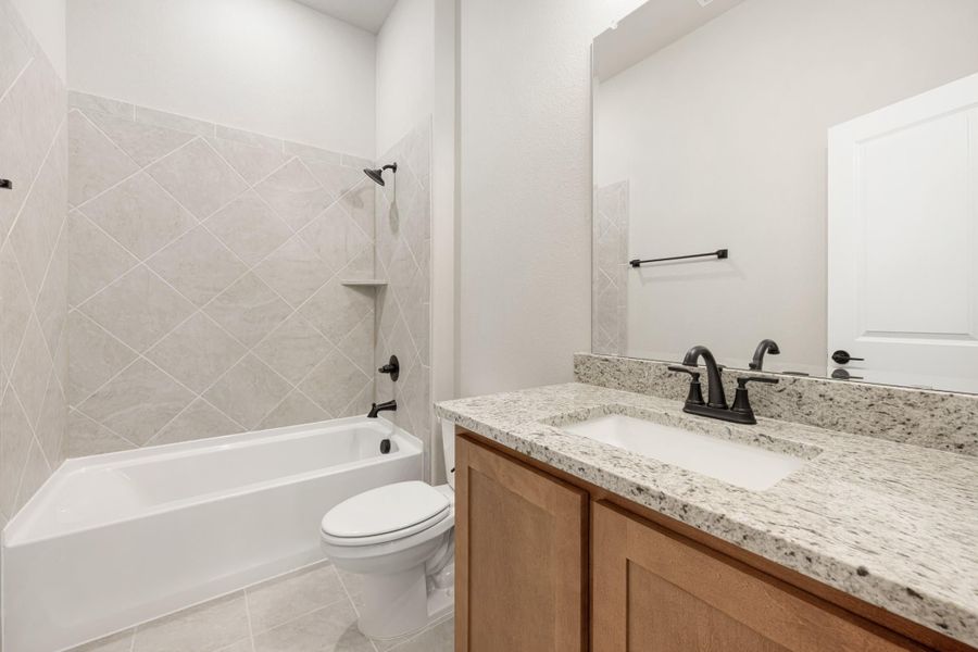 Bathroom with granite vanity, wood cabinets, tub-shower combo, and diagonal tile surround with black fixtures.