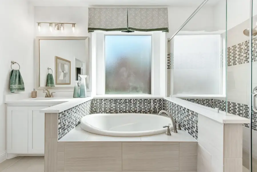 Bathroom with soaking tub, mosaic tile surround, white vanity, and glass shower enclosure