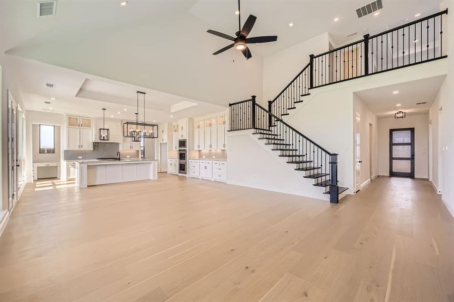 Living room with a towering ceiling, iron spindle staircase, light hardwood / wood-style flooring, sink, and a raised ceiling