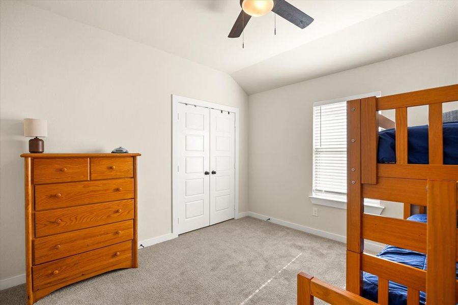 Bedroom with light colored carpet, vaulted ceiling, a closet, and a ceiling fan