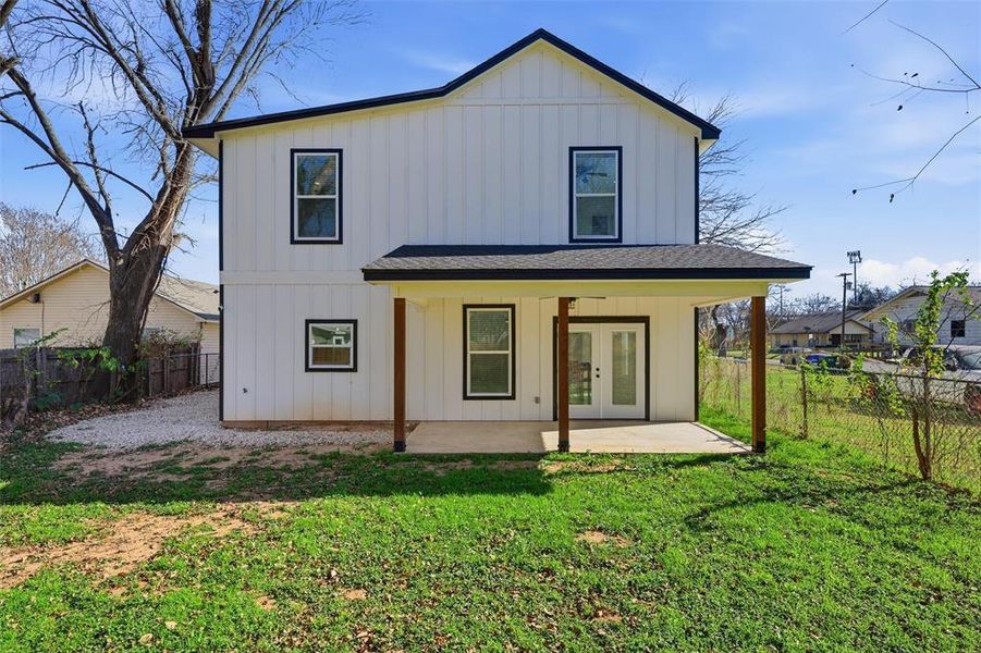 Rear view of house with board and batten siding, a fenced backyard, french doors, a patio area, and a shingled roof Rear view of house with board and batten siding, a fenced backyard, french doors, a patio area, and a shingled roof