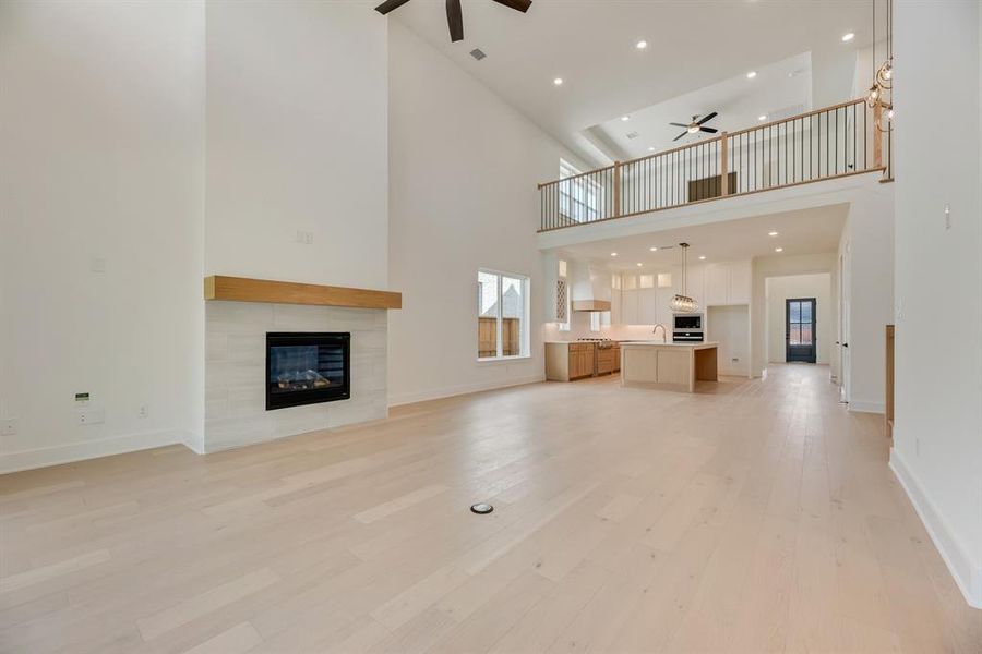 Unfurnished living room featuring ceiling fan, recessed lighting, a tiled fireplace, light wood-style floors, and a high ceiling Unfurnished living room featuring ceiling fan, recessed lighting, a tiled fireplace, light wood-style floors, and a high ceiling