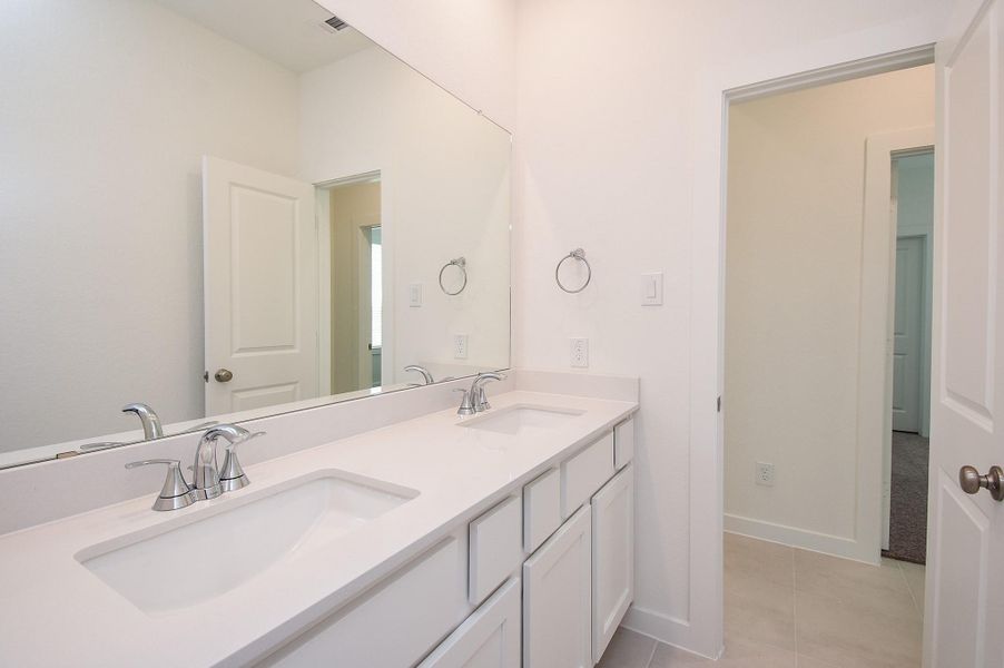 A secondary bath with hallway access, offers dual sinks, good handy storage below, wall-wide mirror and delicate lighting.