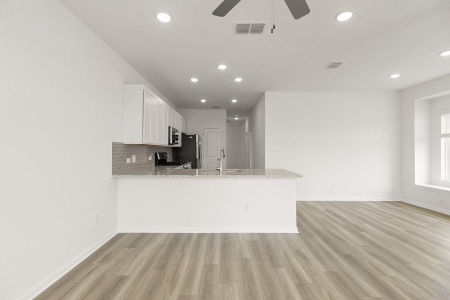 Kitchen with a peninsula, a ceiling fan, white cabinets, light stone counters, and light wood-style floors
