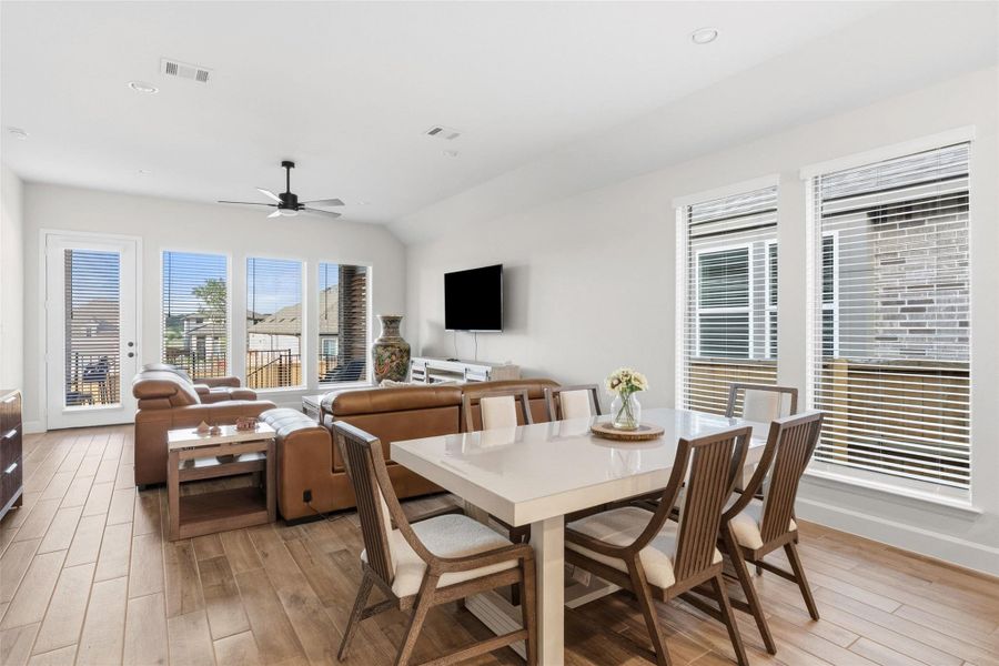Open-concept living area featuring wood-finish flooring, a contemporary ceiling fan, and multiple windows with horizontal blinds