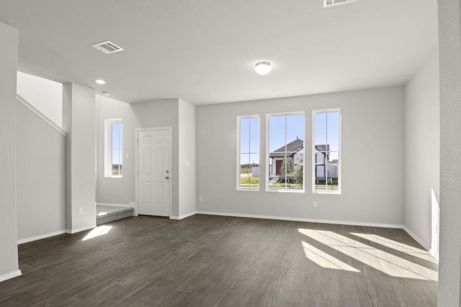 Image of a living room with light grey walls, dark brown vinyl flooring, three windows, and a staircase