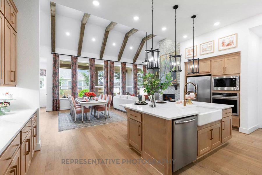 Kitchen with beam ceiling, light wood-style floors, decorative light fixtures, stainless steel appliances, and light brown cabinets