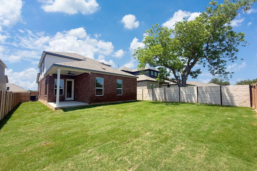 Spacious backyard featuring a covered patio, manicured lawn, and a mature shade tree