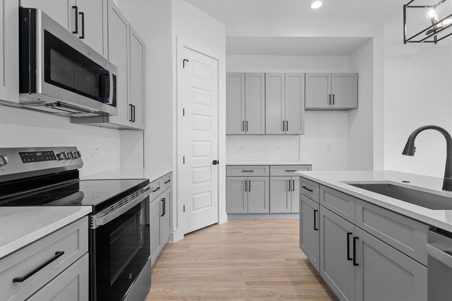 Kitchen with appliances with stainless steel finishes, gray cabinets, light wood finished floors, decorative backsplash, and recessed lighting Kitchen with appliances with stainless steel finishes, gray cabinets, light wood finished floors, decorative backsplash, and recessed lighting