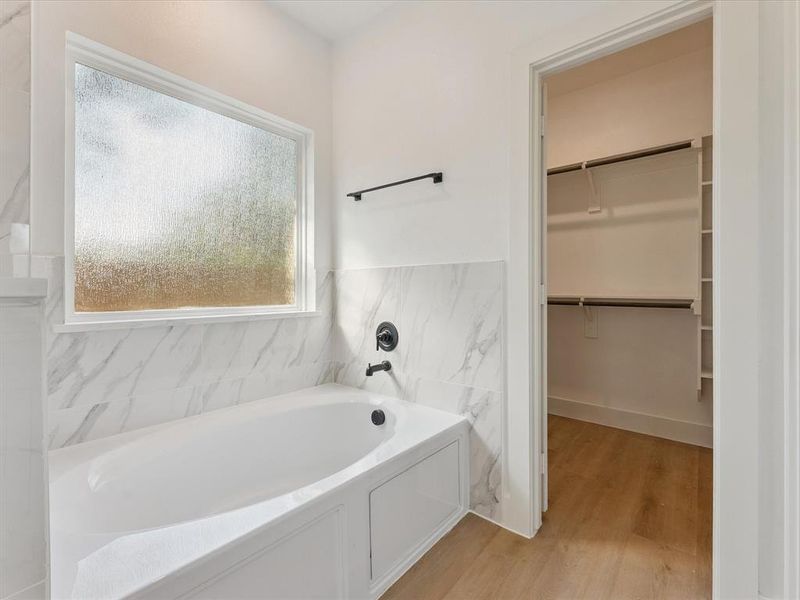 Bathroom featuring a bath, a walk in closet, light wood-type flooring, tile walls, and a wainscoted wall