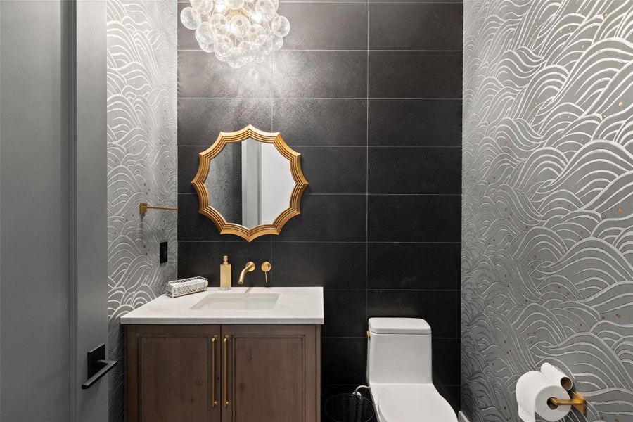 Modern powder room featuring a floating wood-finish vanity with a single basin sink, gold-toned wall-mounted faucet, and a decorative gold-framed mirror
