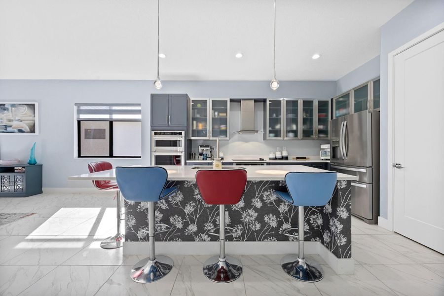 Kitchen featuring decorative light fixtures, a kitchen bar, stainless steel appliances, glass insert cabinets, and recessed lighting