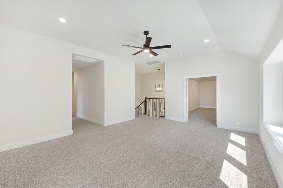 Spacious upstairs loft with gray carpet, ceiling fan, and open staircase landing visible in background.