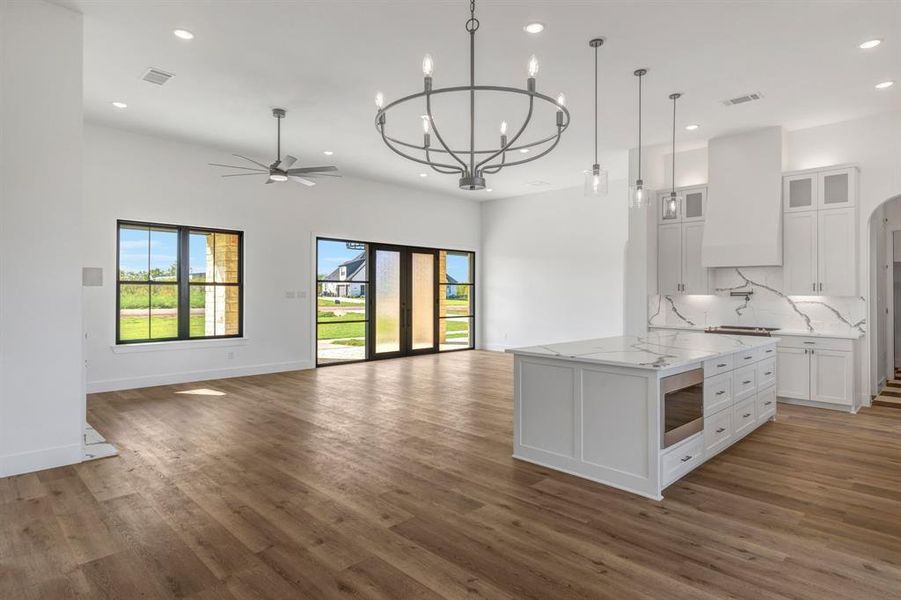 Kitchen featuring glass insert cabinets, open floor plan, a kitchen island, white cabinetry, and pendant lighting