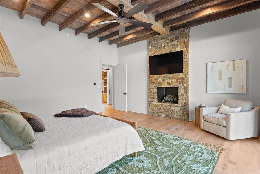 Bedroom with a wooden ceiling with exposed beams, a stone fireplace, and wood finished floors