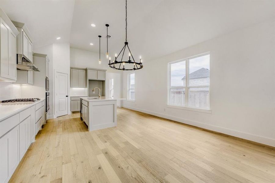 Kitchen with hanging lights, light wood-style floors, a kitchen island with sink, decorative backsplash, and lofted ceiling Kitchen with hanging lights, light wood-style floors, a kitchen island with sink, decorative backsplash, and lofted ceiling