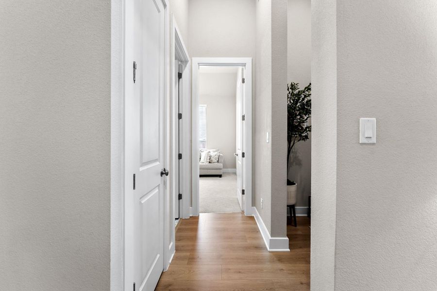 Hallway featuring wood-finish flooring, light neutral-toned walls, white trim, and white paneled doors with black hardware
