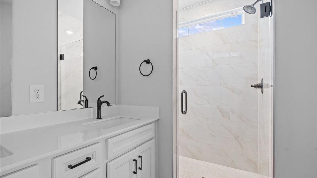 Elegant primary bathroom featuring a spacious tiled walk-in shower and dual vanity in this first-class DRB Homes design