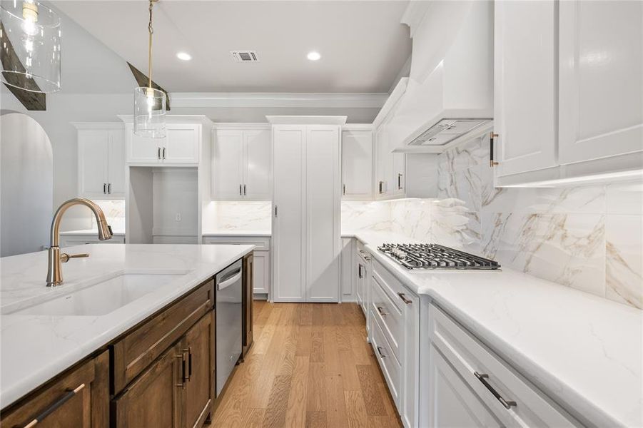 Kitchen featuring light wood-style floors, dual tone cabinetry, backsplash, light stone countertops, and stainless steel appliances
