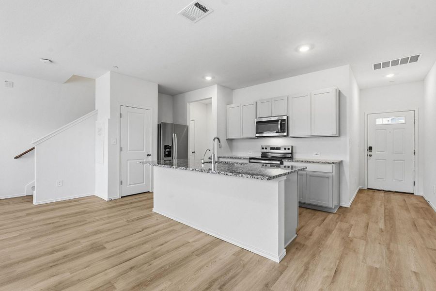 Open-concept kitchen featuring an island with a breakfast bar, stainless steel appliances, granite countertops, and light gray cabinetry Open-concept kitchen featuring an island with a breakfast bar, stainless steel appliances, granite countertops, and light gray cabinetry