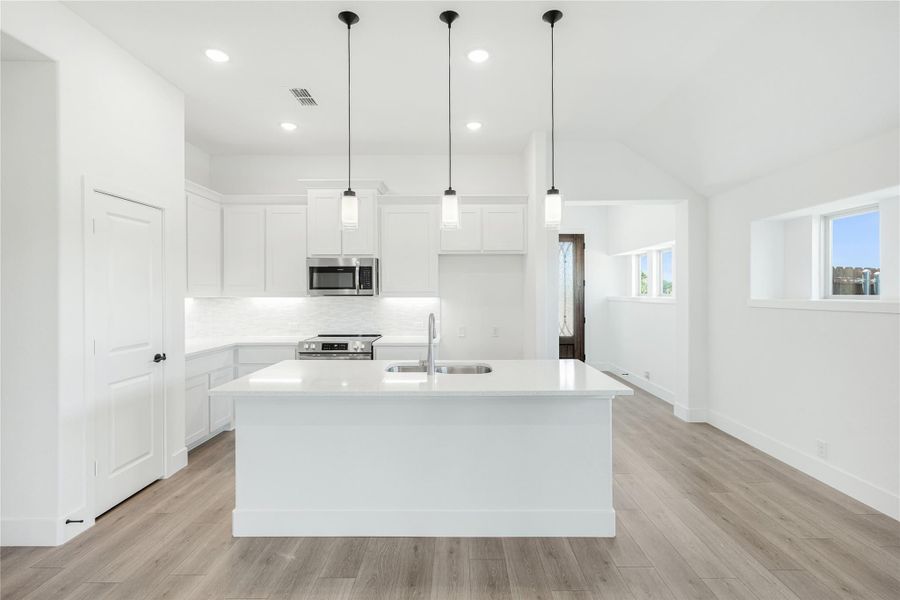 White kitchen with large center island, pendant lights, stainless appliances, and light wood floors