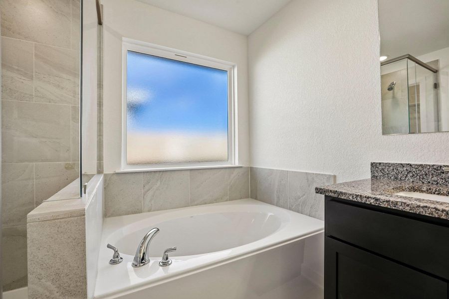 An inviting soaking tub pairs with stone countertops in a modern bathroom design.