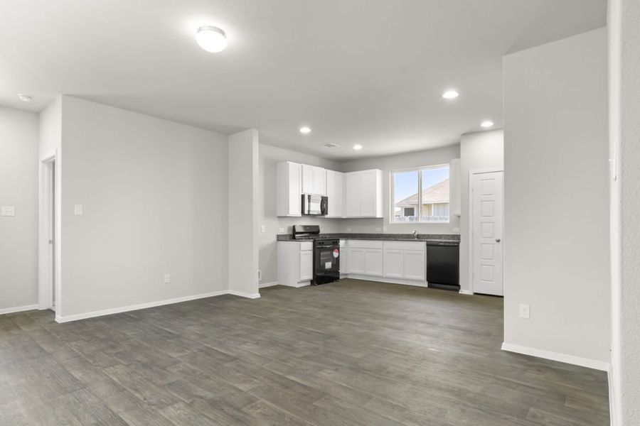 An image of kitchen with wood vinyl flooring, white cabinets with grey countertops, black appliances, a pantry, and cream colored painted walls.