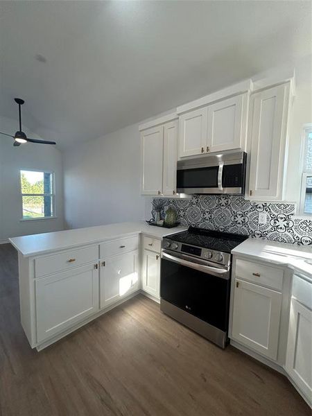 Kitchen with stove, dark wood-type flooring, decorative backsplash, kitchen peninsula, and white cabinetry