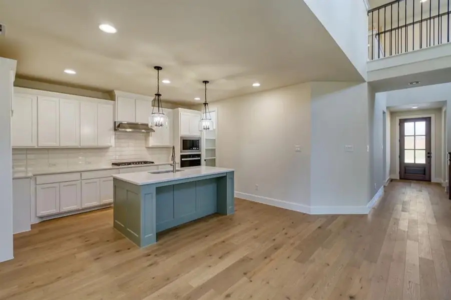 Dual tone kitchen featuring an island with sink, light wood-type flooring, tasteful backsplash, two tone cabinets, and decorative light fixtures Dual tone kitchen featuring an island with sink, light wood-type flooring, tasteful backsplash, two tone cabinets, and decorative light fixtures
