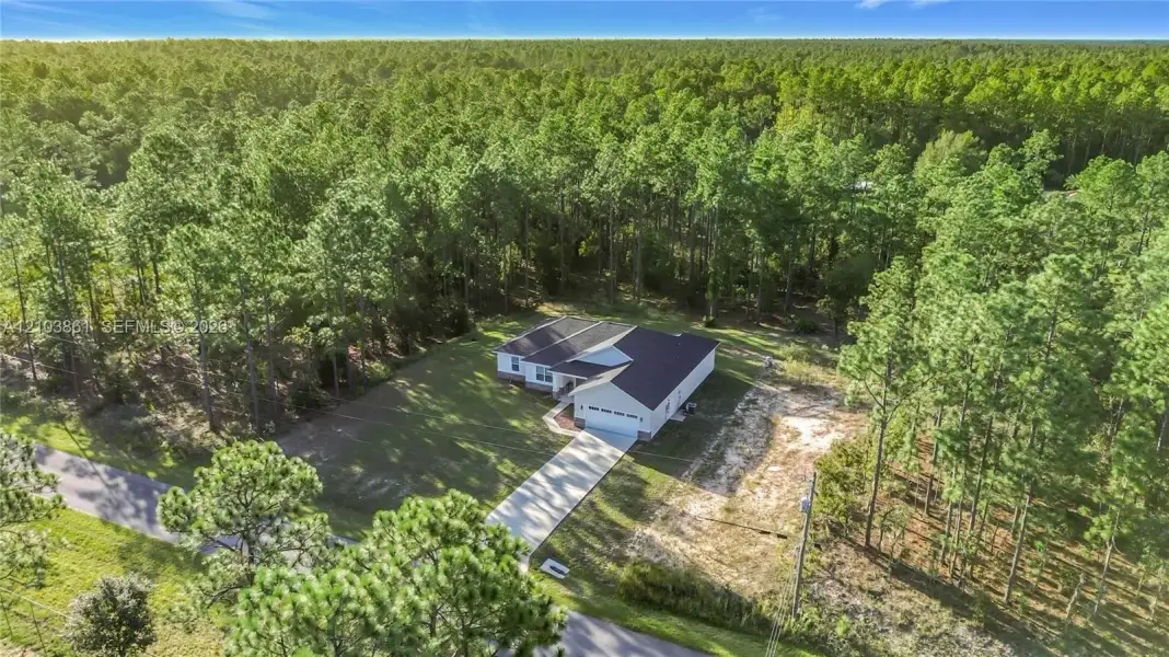Single-story residence featuring a multi-gabled roofline, concrete driveway, two-car garage, and a lot bordered by mature coniferous woodland