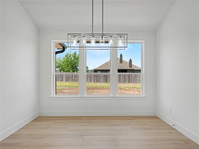 Dining area featuring a contemporary linear chandelier, three large windows, wood-finish flooring, white walls, and white trim Dining area featuring a contemporary linear chandelier, three large windows, wood-finish flooring, white walls, and white trim
