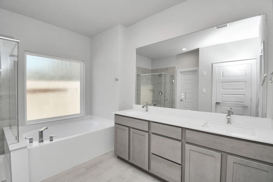Escape to a spa-like oasis in this primary bathroom. Enjoy a walk-in shower with tile surround, a separate garden tub with custom detailing, and an elegant vanity featuring light countertops, modern hardware, and beautiful recessed lights. Experience luxury and relaxation in every detail. Sample photo of completed home with similar floor plan. Actual colors and selections may vary. Escape to a spa-like oasis in this primary bathroom. Enjoy a walk-in shower with tile surround, a separate garden tub with custom detailing, and an elegant vanity featuring light countertops, modern hardware, and beautiful recessed lights. Experience luxury and relaxation in every detail. Sample photo of completed home with similar floor plan. Actual colors and selections may vary.