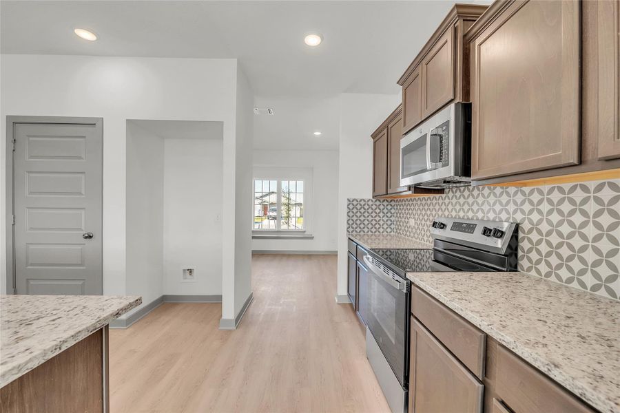 Kitchen with stainless steel appliances, light stone countertops, decorative backsplash, recessed lighting, and light wood-style flooring
