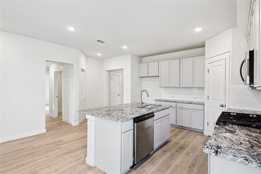 Kitchen with a center island with sink, appliances with stainless steel finishes, backsplash, and light hardwood / wood-style floors