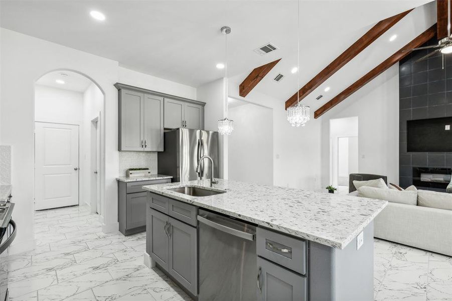 Kitchen featuring pendant lighting, light tile patterned floors, vaulted ceiling with beams, stainless steel appliances, and sink