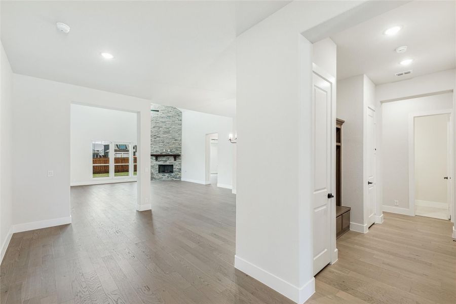 Open-concept living area with hardwood floors, stone fireplace, and mudroom entry visible in hallway. Open-concept living area with hardwood floors, stone fireplace, and mudroom entry visible in hallway.